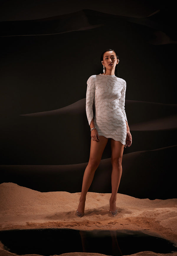 Layers of glimmering threadwork combined with white sequins finish this captivating asymmetrical dress. This figure-skimming, stretchable mini dress in lycra net features a scallop high-neck and hem along with long sleeves for an elevated look. Complete your look with strappy sandals and minimal jewellery.