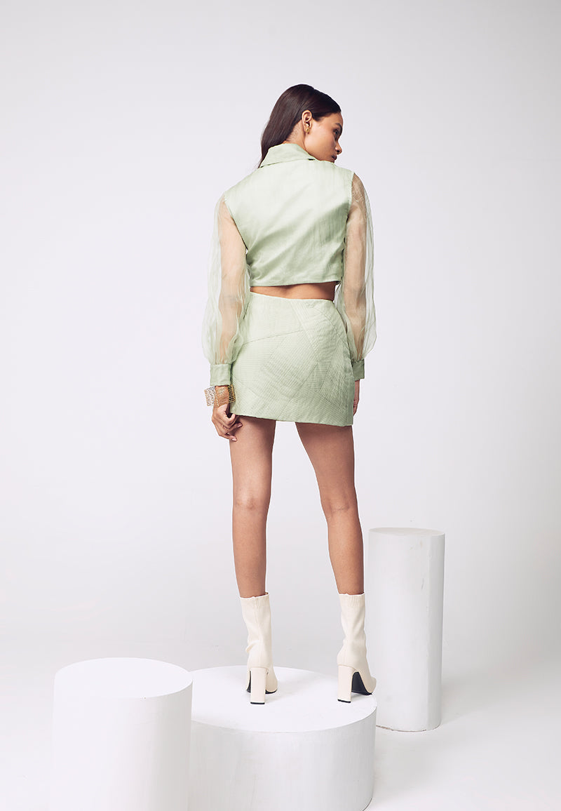 Opt for pastels this summers to brighten the mood. This cotton satin co-ord set in pastel green layered with organza, with hand-pleated details, is a must-have. The shirt features a spread collar with poofy organza sleeves and thigh-slit mini skirt comes in a wrap around style. Pair it with minimal gold jewelry for your next big event or night out.
