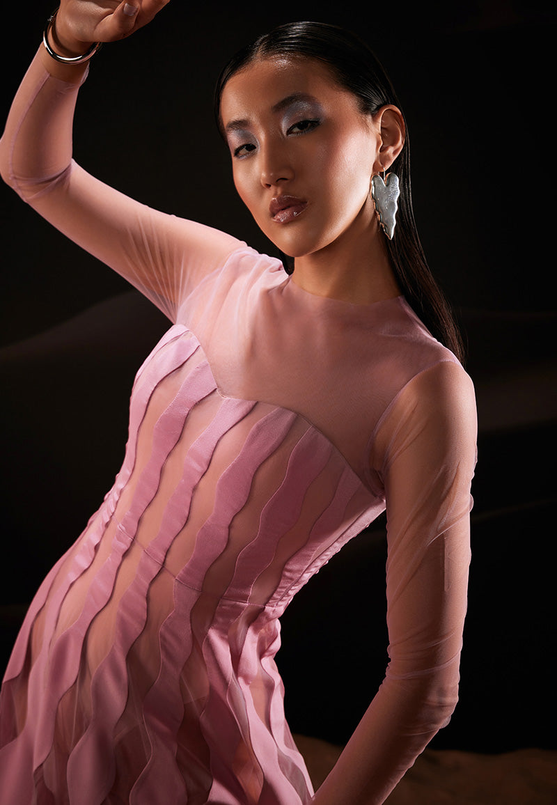 Geometric scallop-shaped patterns in crepe and net are cut and patched together in this flared, ankle-length dress in pastel pink for a feminine structure and appeal. This skillfully designed tailored dress features a round neck and a fitted bodice with an attached bodysuit in nude colour. Long sheer net sleeves are added to complete the look. Concealed zipper is attached at the center back for closure. Pair it with translucent pumps and minimal jewellery for your next formal dinner.