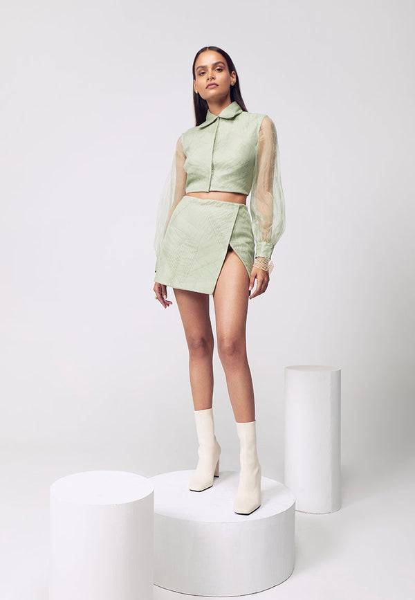 Opt for pastels this summers to brighten the mood. This cotton satin co-ord set in pastel green layered with organza, with hand-pleated details, is a must-have. The shirt features a spread collar with poofy organza sleeves and thigh-slit mini skirt comes in a wrap around style. Pair it with minimal gold jewelry for your next big event or night out.