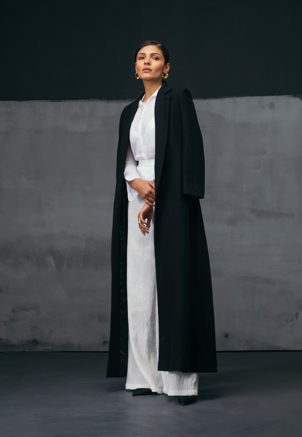 Mannat Gupta's collection of women's coats and jackets. This black collared wool coat comes with pleating on the back creating depth and movement in the piece. The wool coat is floor-length making it perfect to be paired with long dresses and formal attire in the fall and winter. Pair this with a flared pant and top or sweater along with booties and minimal gold jewelry to complete the look 
