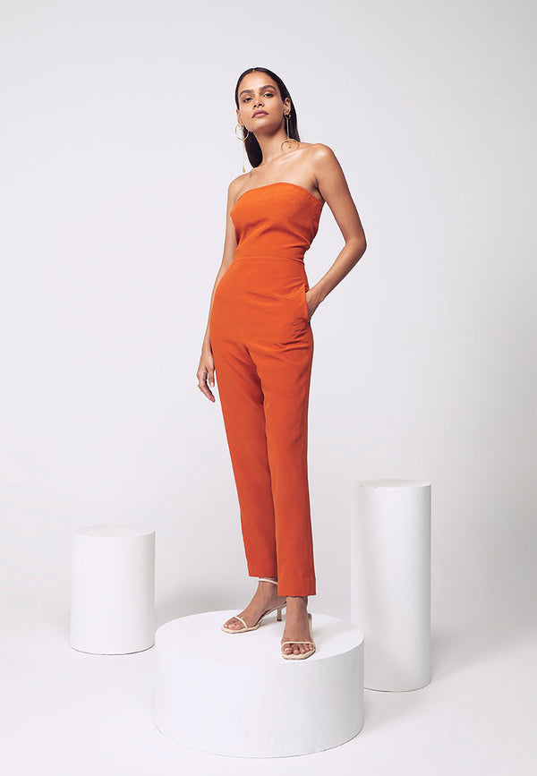 New style figure-hugging jumpsuit. Crafted in pure silk crepe in burnt orange with inseam pockets which are perfect for your next soiree or even a beach party. Easy to wear this ankle-length bodycon jumpsuit comes with a detachable pleated trail with a hook and eye closure for easy access and confort. Create multiple looks for multiple events with detachable, functional clothing. Complete the look with heeled sandals and minimal gold jewelry. 