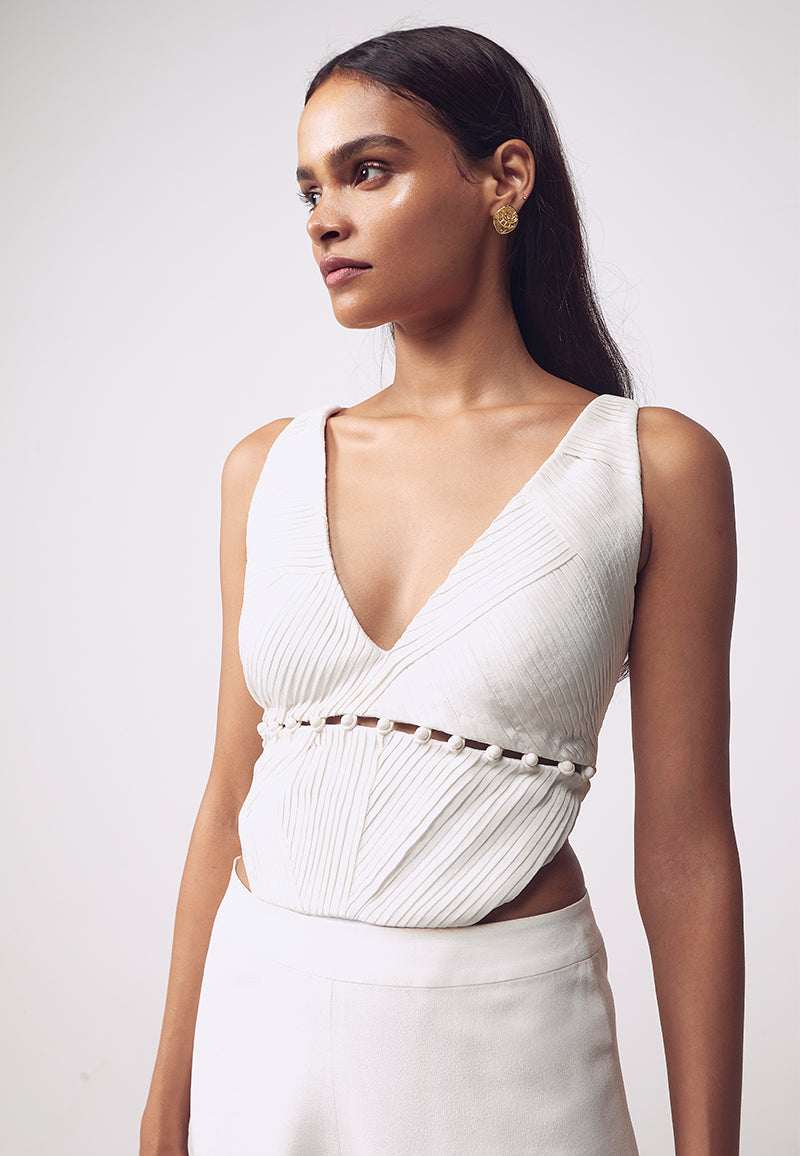 Mannat Gupta's detachable pleated bodysuit is made using silk crepe in white. The sleeveless bodysuit is constructed with asymmetrical pleats and deep V neckline with a bare crossback. This cut-out bodysuit features fabric buttons below the under bust for detachable functionality to create multiple looks. The bodysuit can be turned into a bustier in seconds using the buttons making it look like a different piece completely.