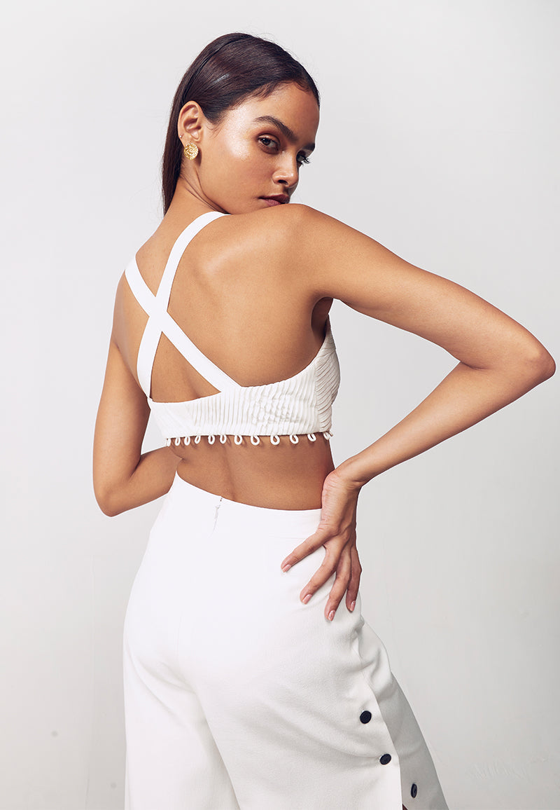 Mannat Gupta's detachable pleated bodysuit is made using silk crepe in white. The sleeveless bodysuit is constructed with asymmetrical pleats and deep V neckline with a bare crossback. This cut-out bodysuit features fabric buttons below the under bust for detachable functionality to create multiple looks. The bodysuit can be turned into a bustier in seconds using the buttons making it look like a different piece completely.