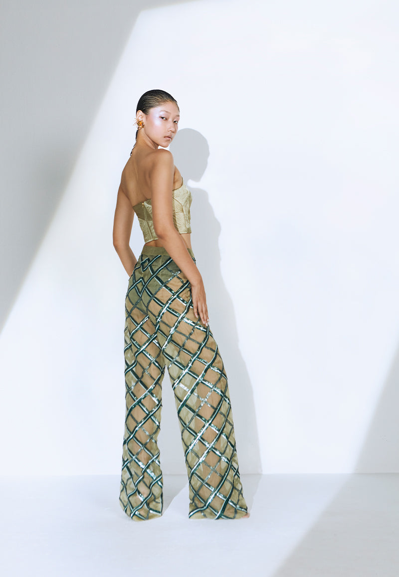 Hand-embroidered on pastel olive green net, the sheer pant features criss-cross embroidery pattern playing with different sequin sizes and colors in green. This transparent pant fall straight to floor from the high-waist. It has a zip closure at center back and comes with a pair of green underpants. Wear it for a fancy dinner party with heeled sandals or pumps and a bustier or corset to complete the look.