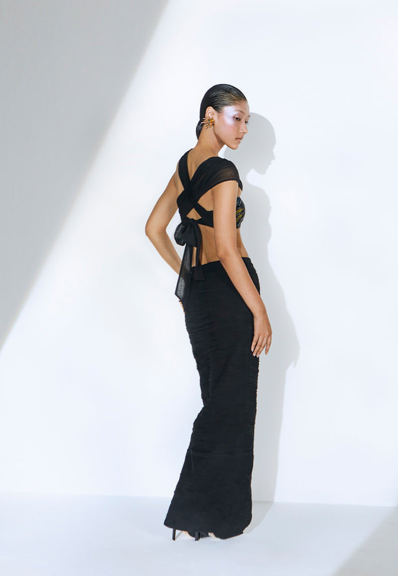 Ruched in lightweight black georgette, this bodycon skirt features an interesting asymmetrical V-shaped waist cut. This black maxi skirt has a zip closure on side seam with a thigh-high slit on the front; it falls till the ankle. Pair it with one of our embellished bustiers, heeled sandals and minimal gold jewelry to complete the look.