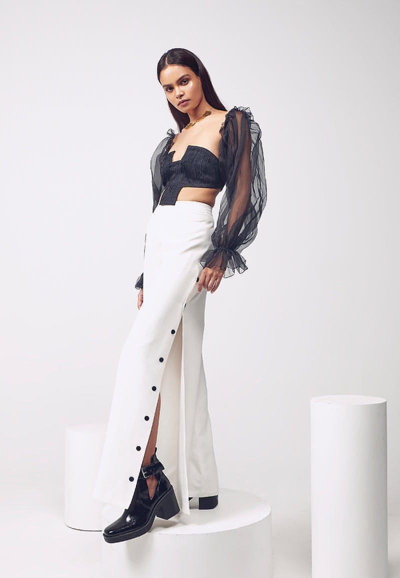 Add a dose of glamour with these high-waisted pants in white. This thigh-high slit flared pants with black buttons can be worn for different occasions. Crafted in pure white silk crepe with black buttons as closure on both sides and a concealed zip make it versatile. Wear it in winters or summers for a brunch date or evening look with boots or heels.