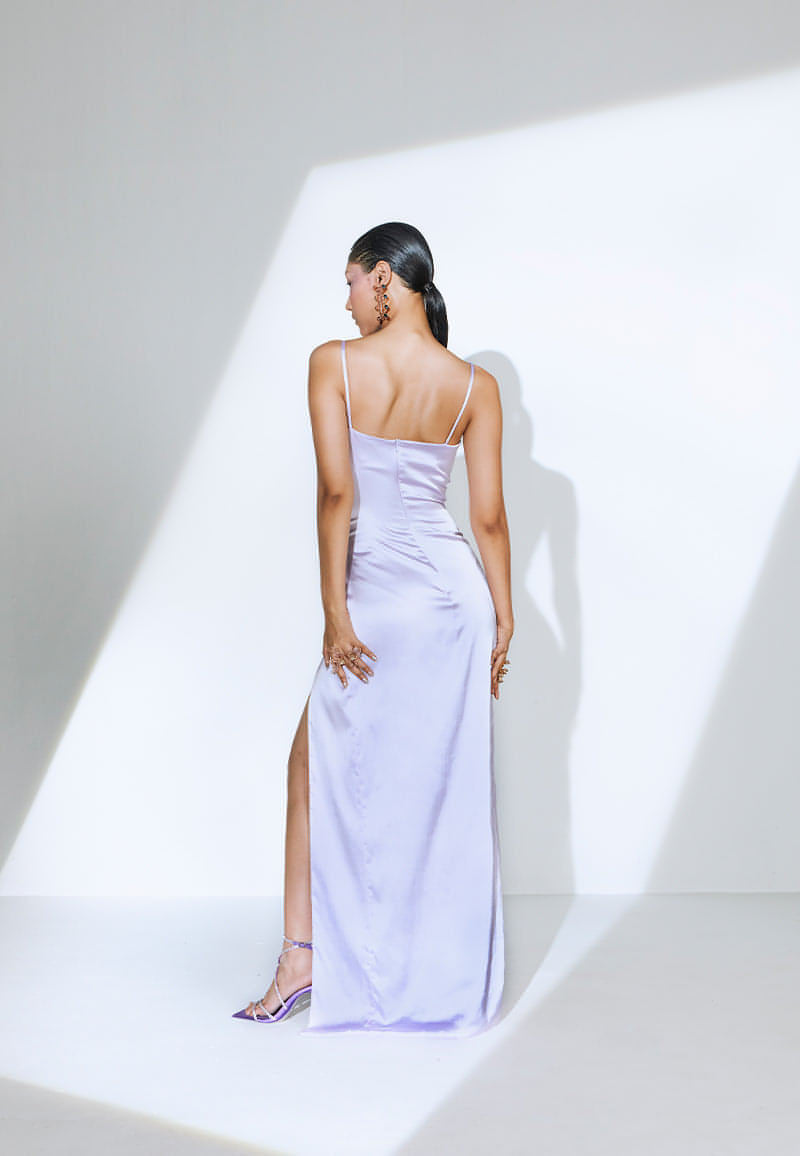 This figure-skimming maxi dress is constructed in lightweight, luxurious lilac satin. The dress features a cowl neckline withan asymmetrical pleating detail from the under bust till the waist. The thigh-high slit on the front is added to accentuate the body. The bodycon long dress has a zip closure at the center back. Wear it for a sophisticated dinner party or cocktail with a pair of heeled sandals or pumps and diamonds.