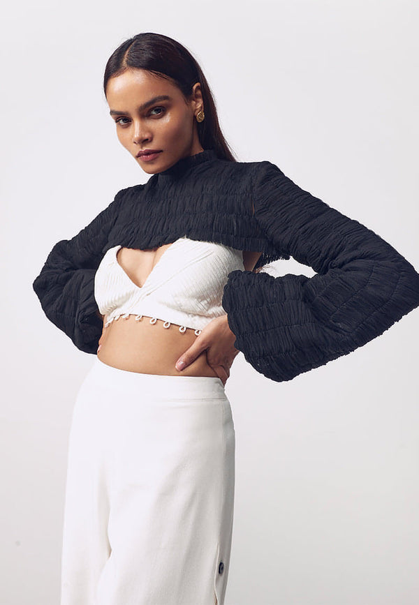 This black puff pleated bust cut crop top is single layered net covered in minuscule handcrafted pleats with elastic thread. The top features ruching detail on the neck with a concealed zip closure. Style it in summers or winters with our white pleated detachable bodysuit and high-waisted pants or our sweetheart tucked mini dress.
