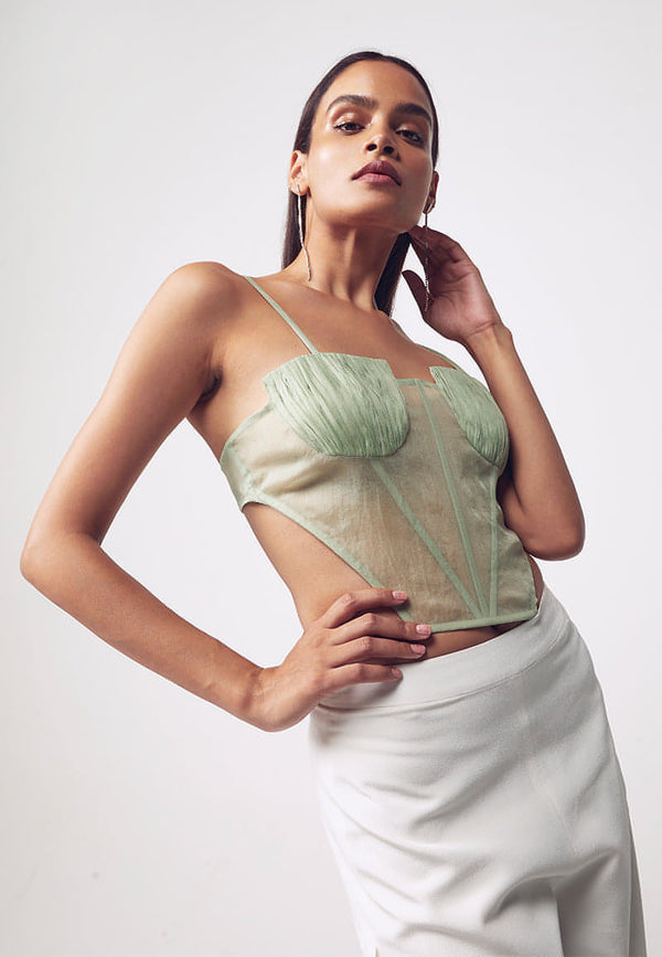 Mannat Gupta's collection of corsets, bustiers and tops. This ruched corset is made with organza in pastel green. This sleeveless, cut-out corset features ruching on the busts with a bare back. Hook and eye closures are attached at center back for seamless comfort. This minimal and versatile corsted top is perfect for any party and to deal with the summer's heat. Pair yours with one of our high-wasited pants or skirts along with heeled sandals to complete your look.  