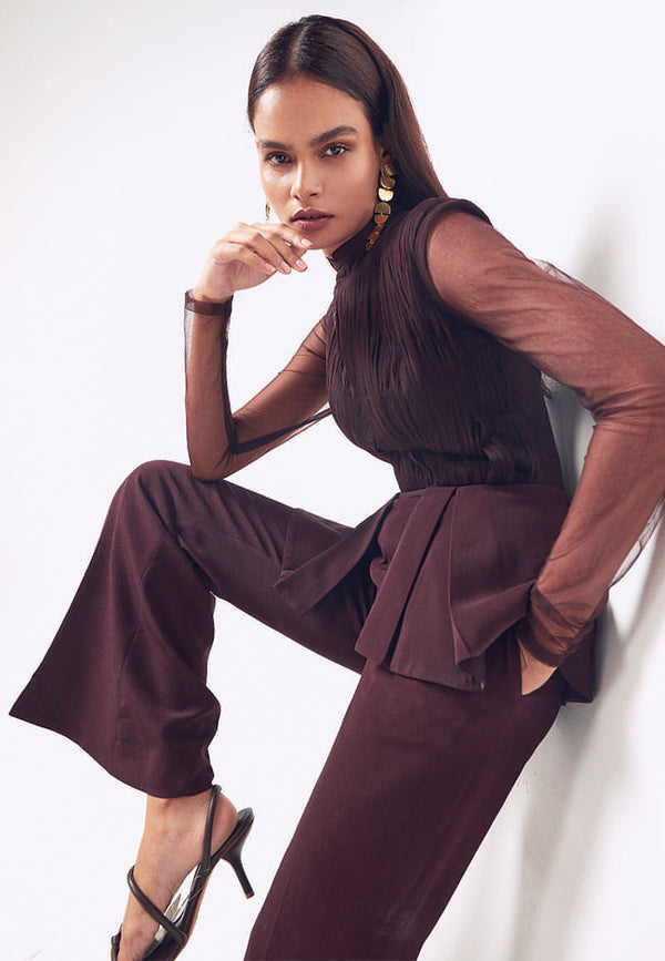 This ruched long sleeved jumpsuit with detachable peplum in wine is a curation for glam winter evenings. Crafted from luxurious silk crepe and fine net, this shoulder-padded detachable peplum jumpsuit is perfect for an evening look. This piece has a Chinese collar, minimal ruching detail on the bodice and boot-cut flared pants with a concealed zip closure at the center back. Wear the jumpsuit without the peplum for a bodycon fit and with the peplum for a comfortable one.  Style it in winters or summers