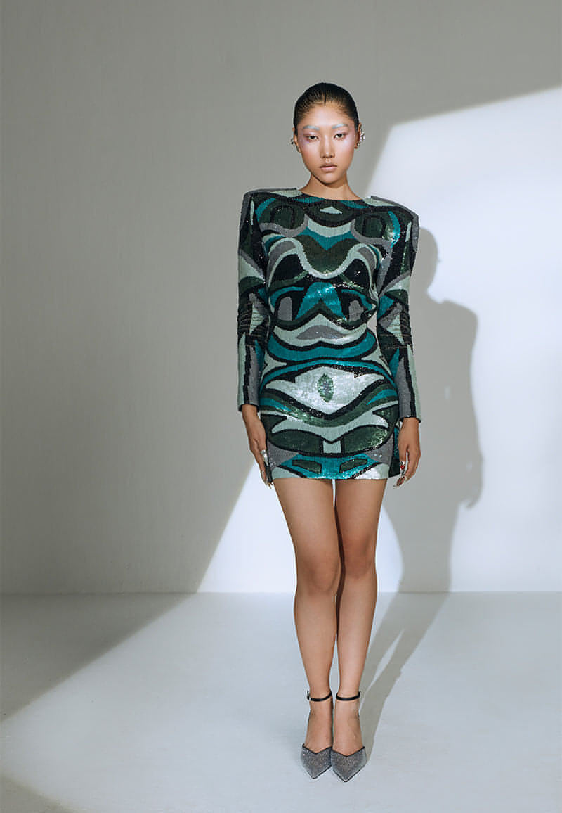This figure-skimming mini dress is covered with pastel sequins and an interesting pattern all over. The dress is padded to create exaggerated shoulders and give that extra bold look. It features a deep V-shaped neckline at the back. This bodycon mini dress comes with long sleeves that are hand-embroidered with sequins too. It has concealed zipper on the side seam. Pair it with strappy heels and minmal silver jewelry to complete the look.