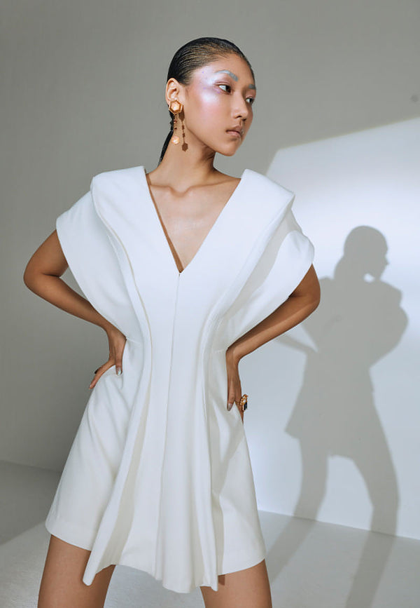 Skillfully tailored in white lycra crepe, this structured mini jacket dress has hooks and eyes as a closure at the center front. The creation is accentuated by adding feather boning from the font of the dress to the back to give it a bold look. This sleeveless dress features an exaggerated cut-out under the armhole to add structure and shape to the piece. Wear it as a jacket or a mini dress with heeled booties or sandals and minimal silver jewelry.