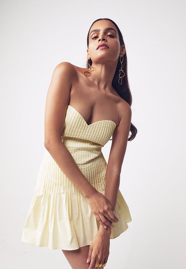 This women's mini dress features couture-inspired details. This buttercream bandeau, bodycon dress features a sweetheart neckline and tuck details on the front for texture and depth, accentuating a woman's body features. This pale yellow mini dress fetures a flared bottom making it perfect for Sunday brunches and birthdays. Pair yours with minimal gold jewelry and heeled sandals to complete the look.